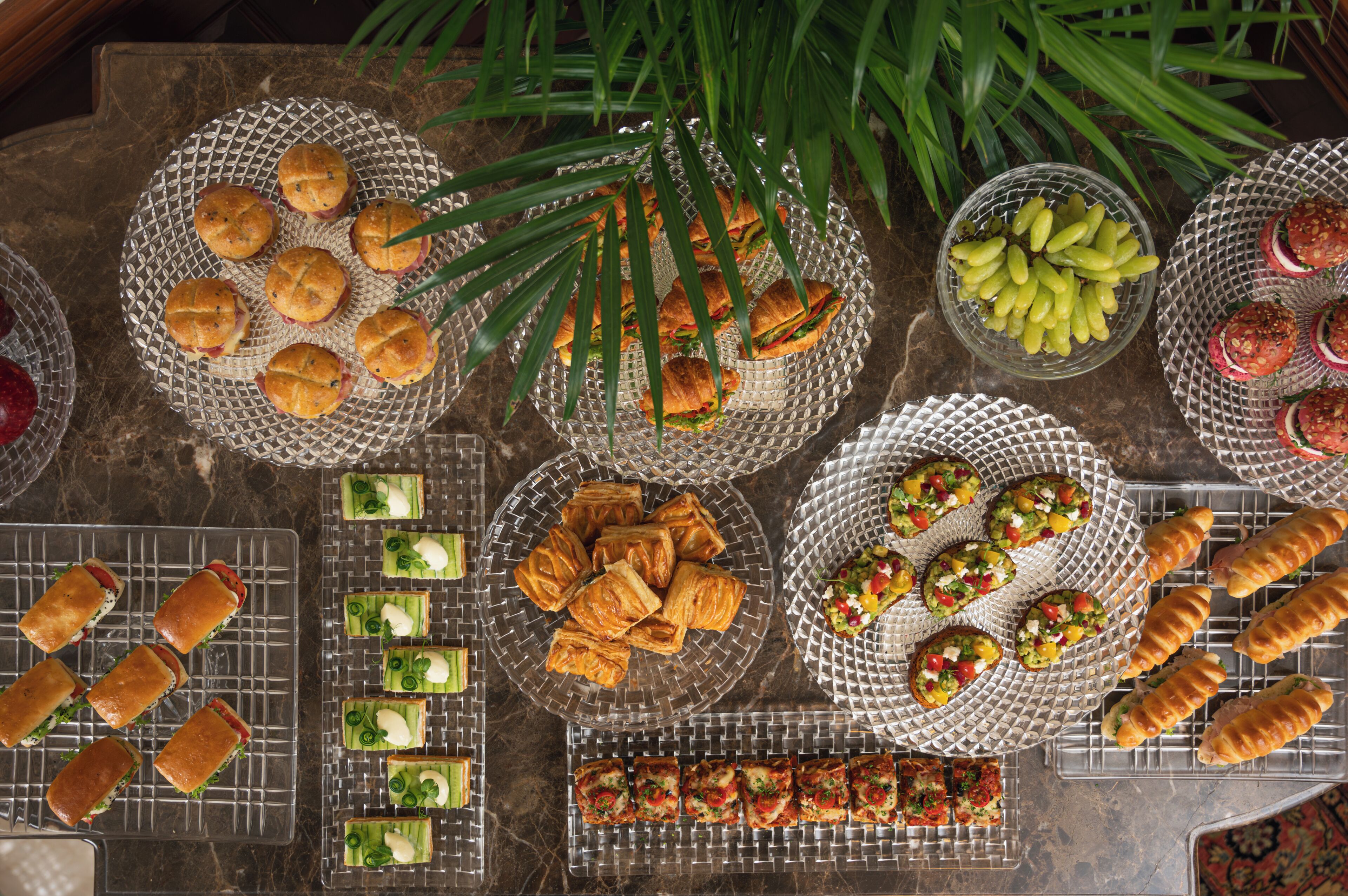 Variedad de alimentos en bandejas y platos, incluyendo sándwiches, pasteles y aperitivos.