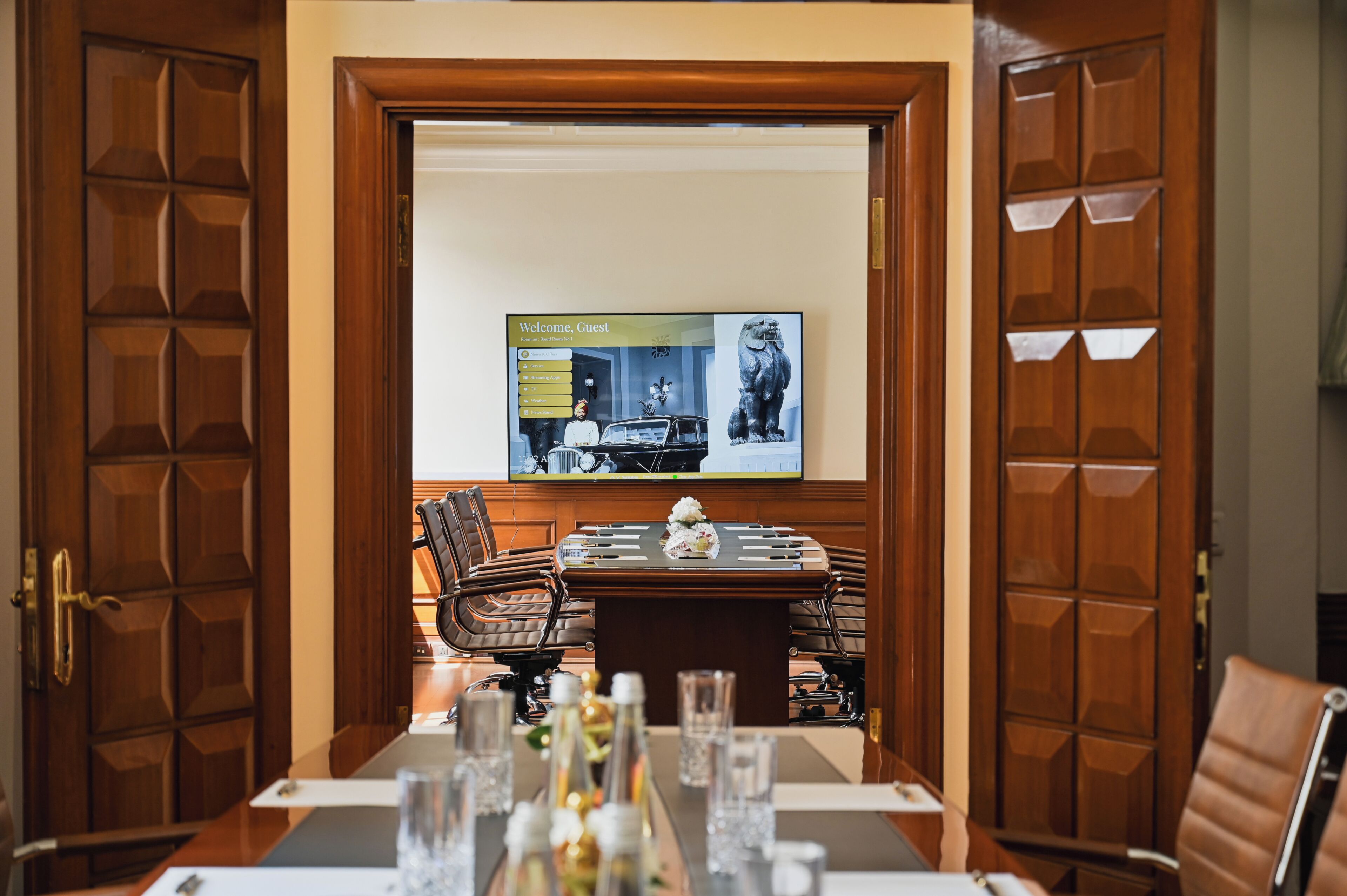 A conference room with a wooden table, chairs, and a television screen displaying a welcome message.
