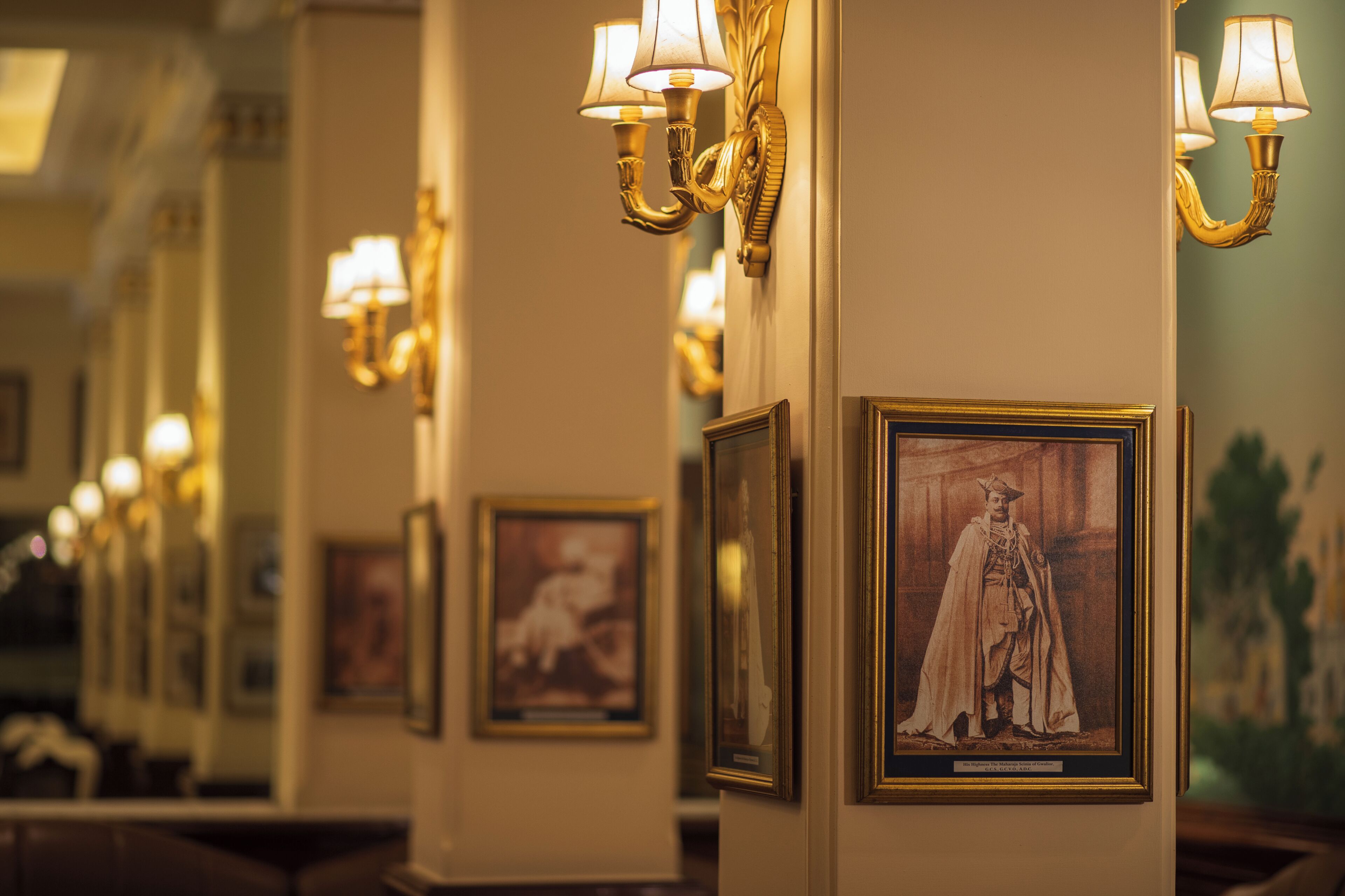 A corridor with framed portraits on the walls and wall-mounted lamps.