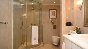 A modern bathroom with a glass-enclosed shower, a white toilet, and a marble bathtub.