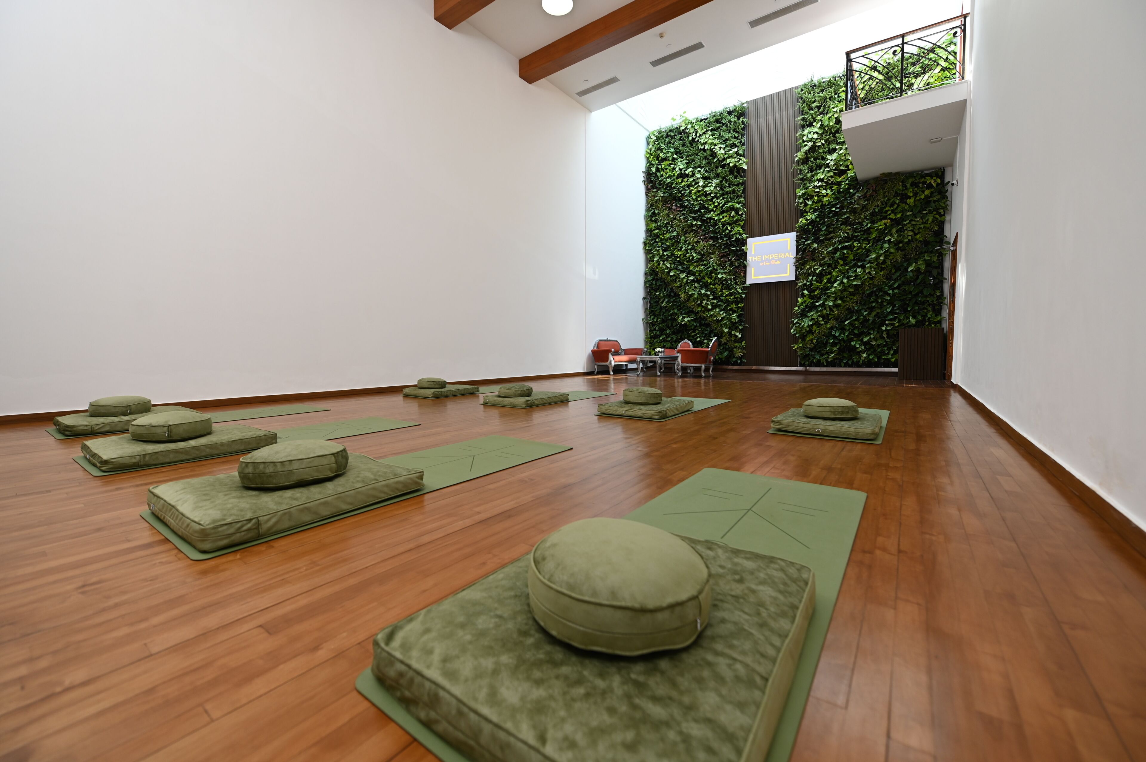 A room with wooden flooring, green mats, and cushions arranged for a yoga or meditation session.