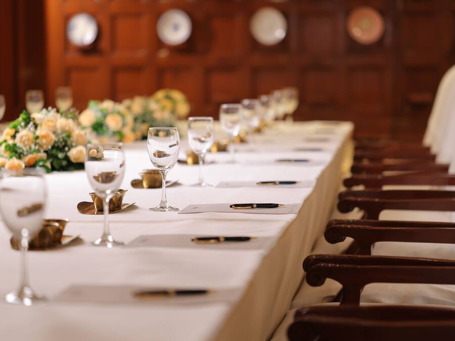 Una larga mesa de comedor con sillas, vasos y un centro de mesa floral.