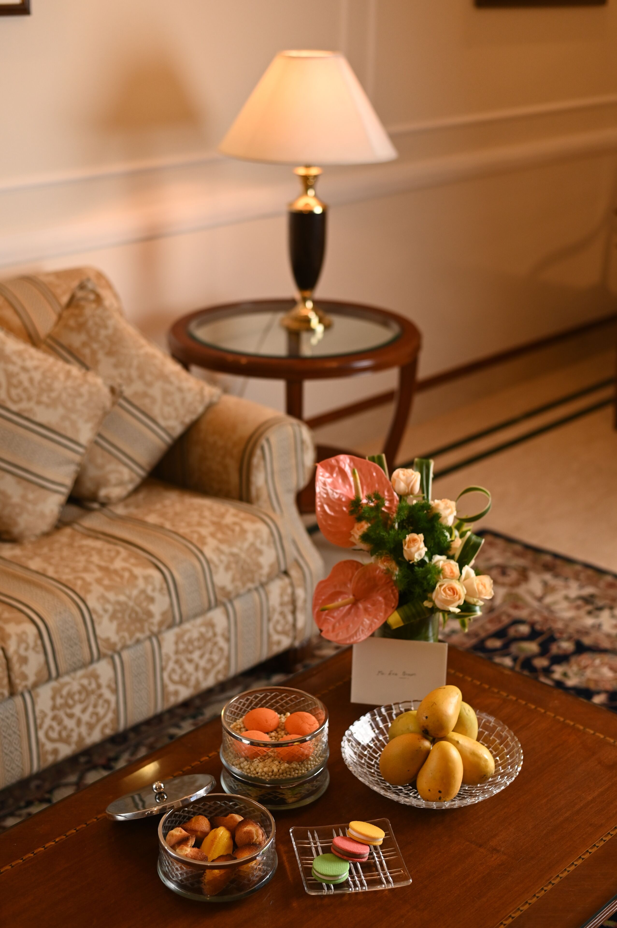 A living room with a sofa, a table with decorative items, a lamp, and a floral arrangement.