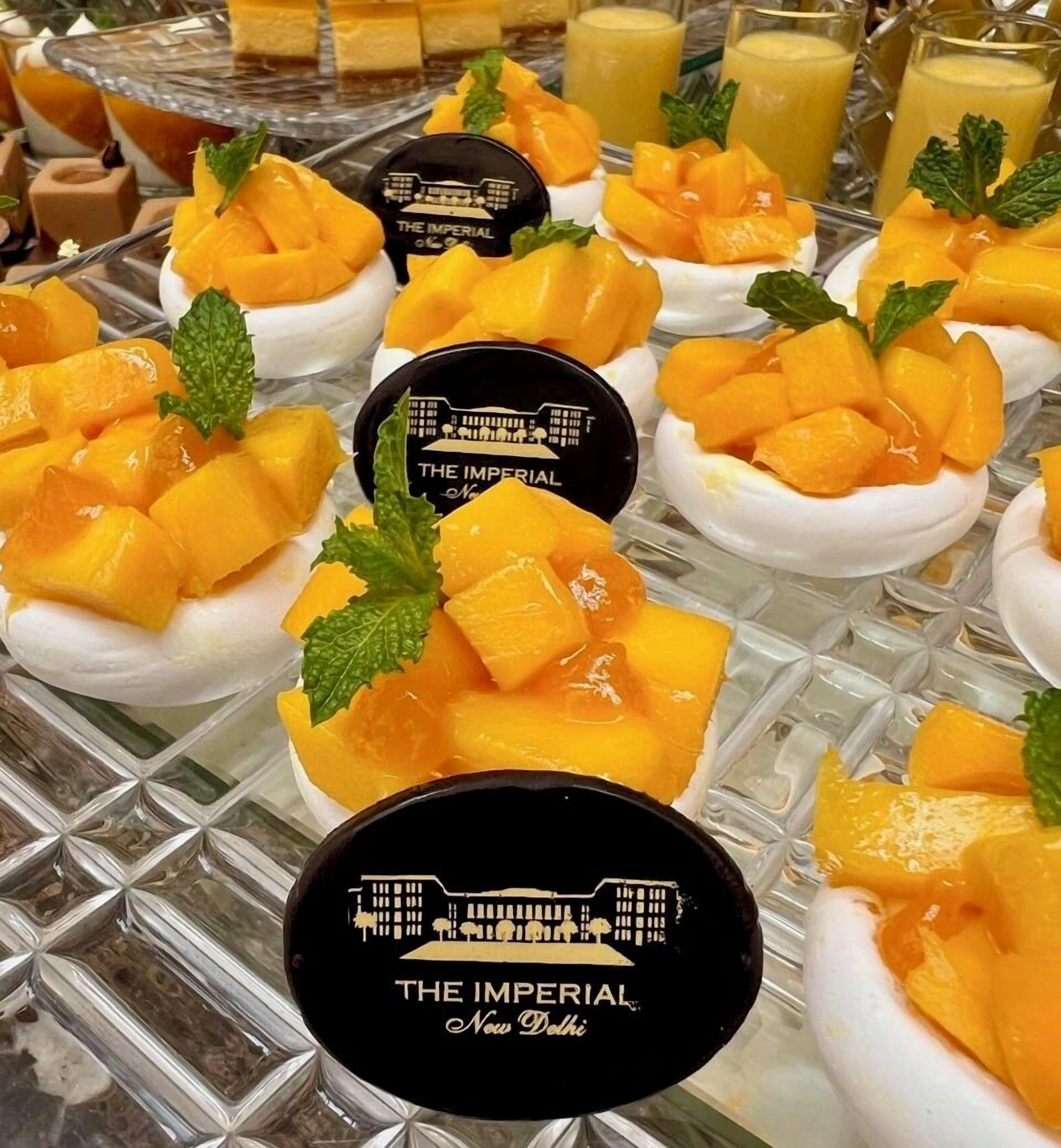 A dessert display with mango chunks on meringue bases, mint leaves, and branded containers.