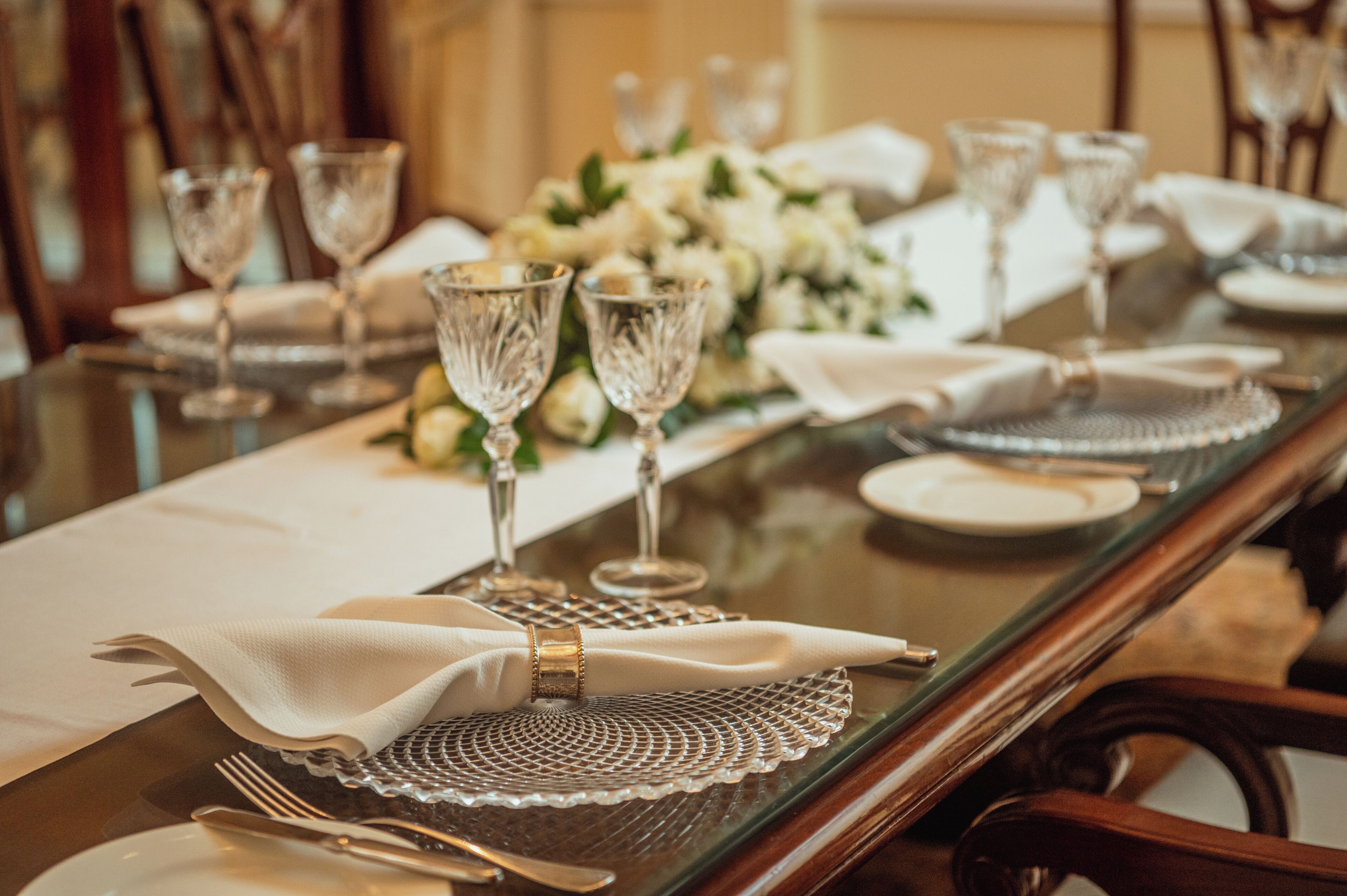 A dining table set with crystal glassware, white napkins, and a centerpiece of white flowers.