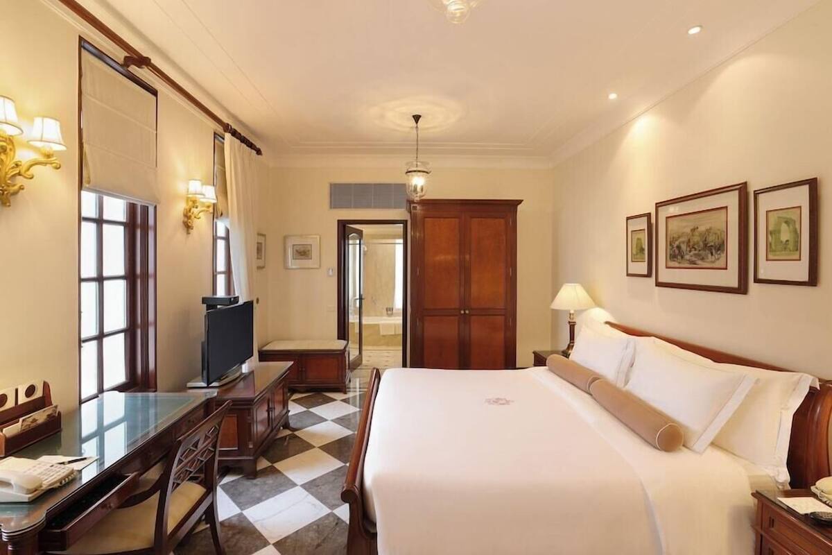 A hotel room with a bed, desk, chair, television, and artwork on the walls.