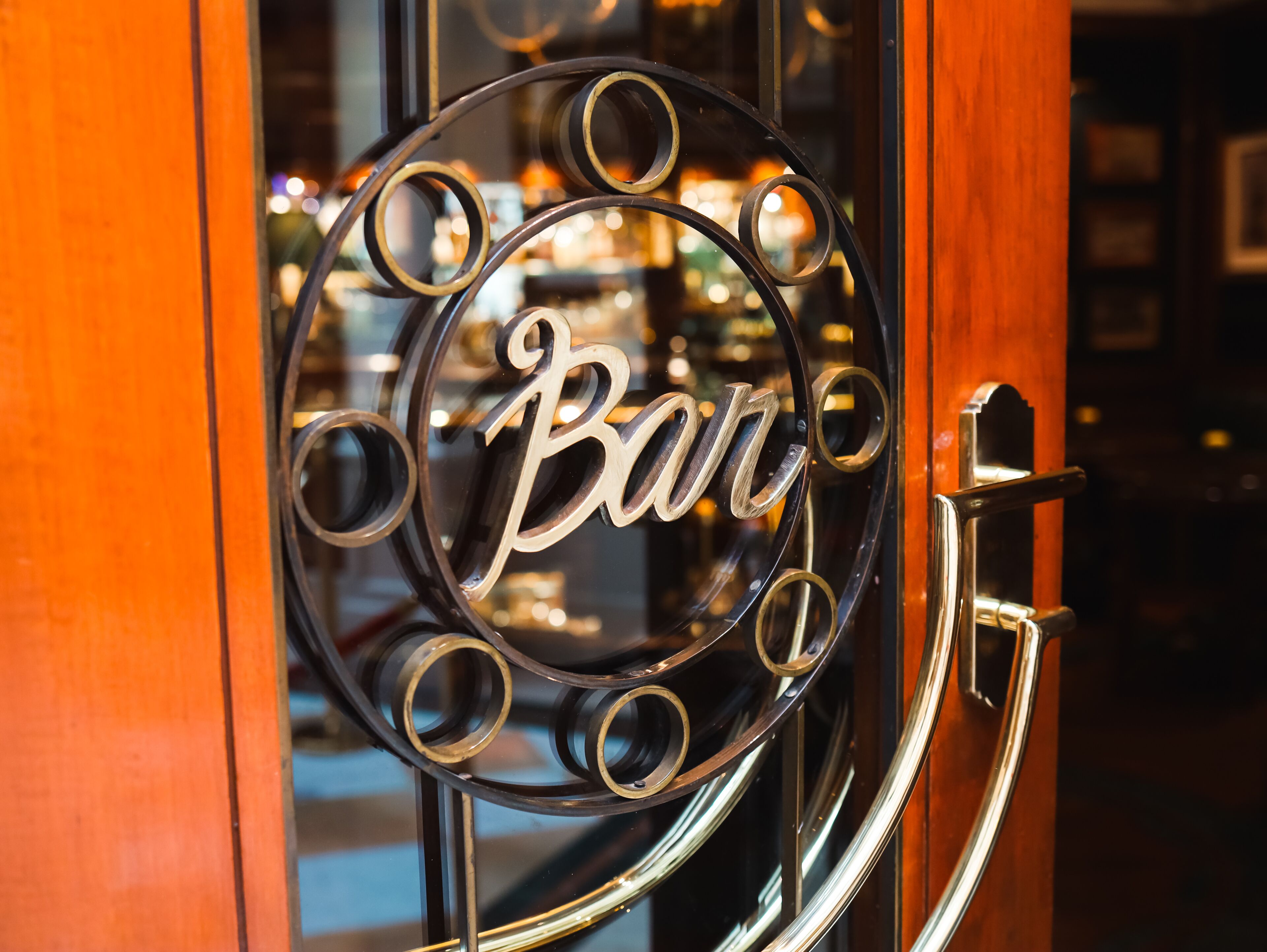 A door with a circular metal sign featuring the word 'Bar' in a decorative font.
