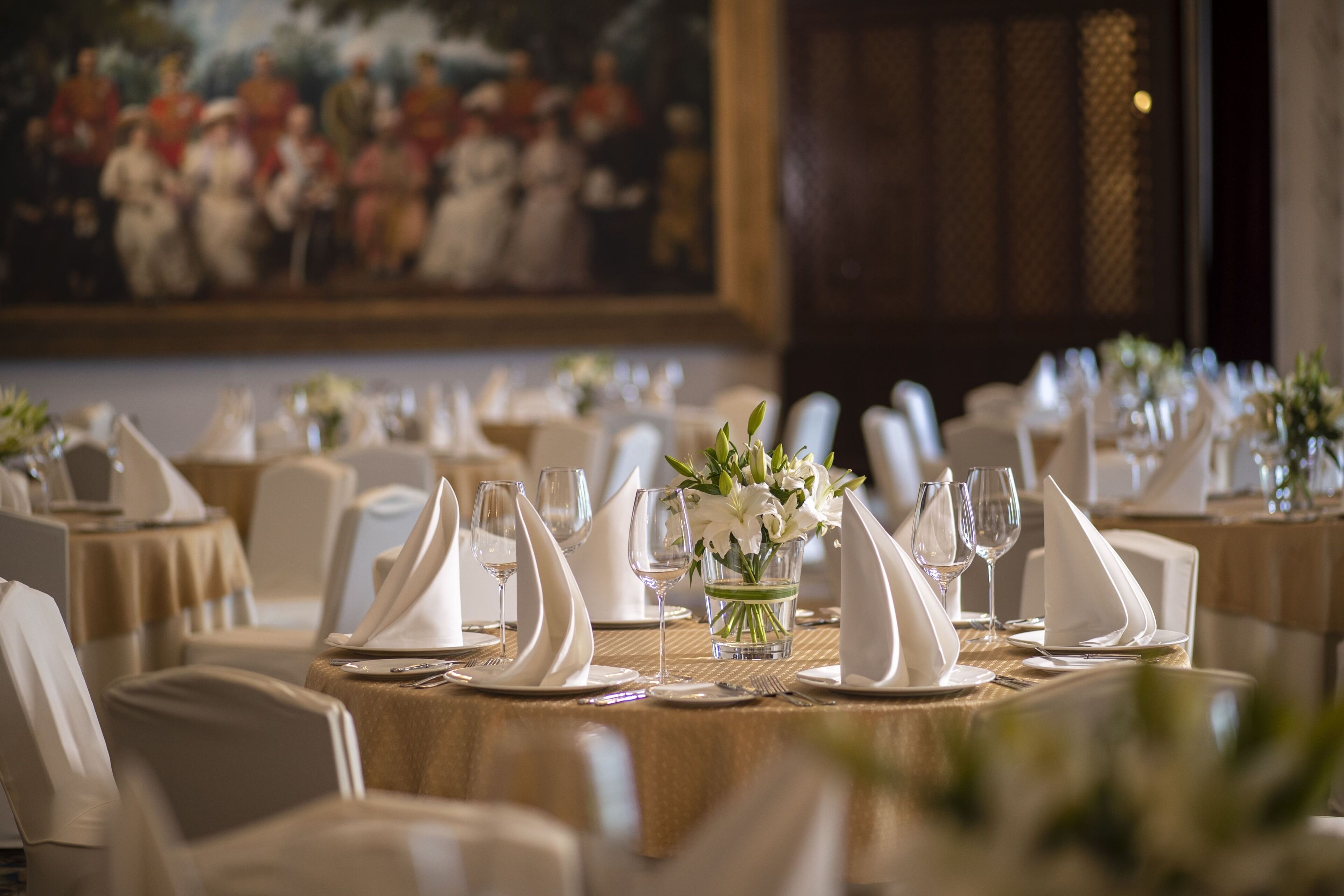 Un comedor formal con mesas dispuestas para el servicio, un cuadro en la pared y un diseño de paneles de madera.