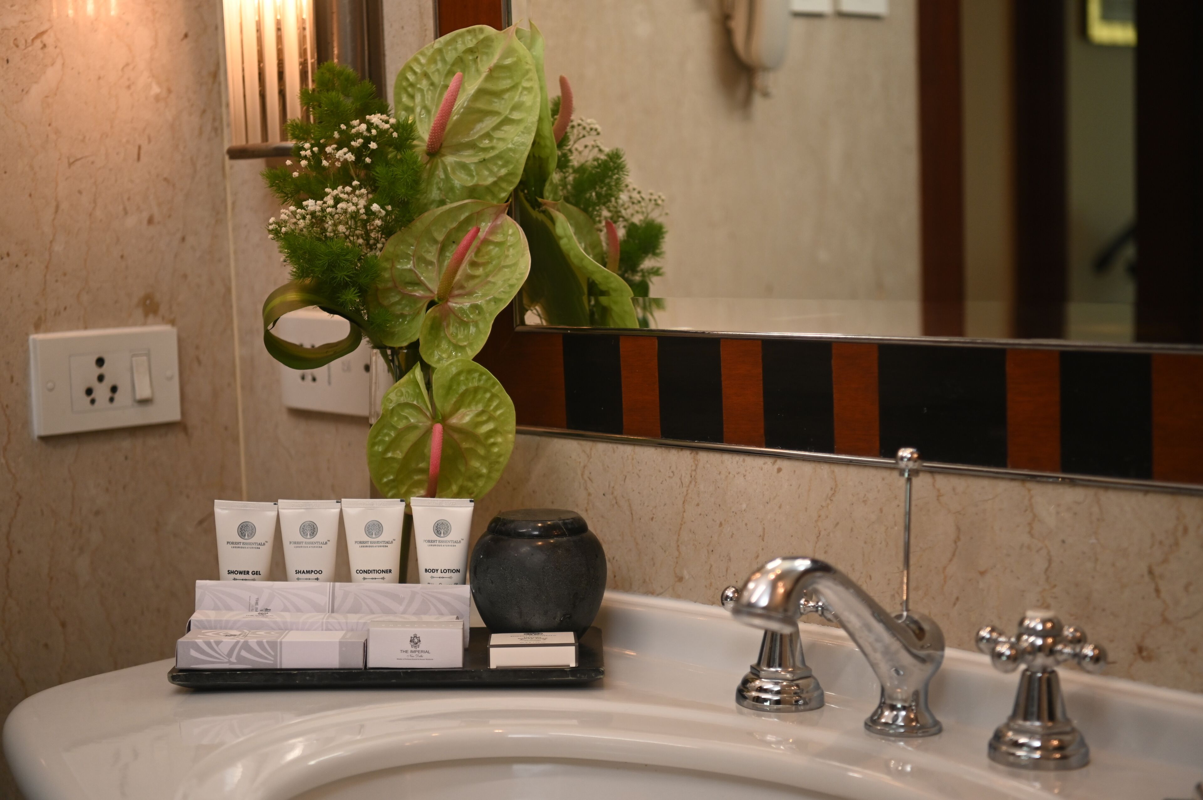 A bathroom sink with toiletries, a vase with flowers, and a mirror.