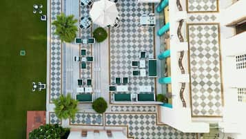 Vue aérienne d’un hôtel dont le sol présente un motif à carreaux, avec des espaces de repos en plein air dotés de parasols et un escalier menant à un étage supérieur.