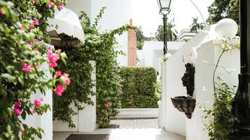 A narrow pathway flanked by white walls, a black lantern, and a white column with a pink flower.