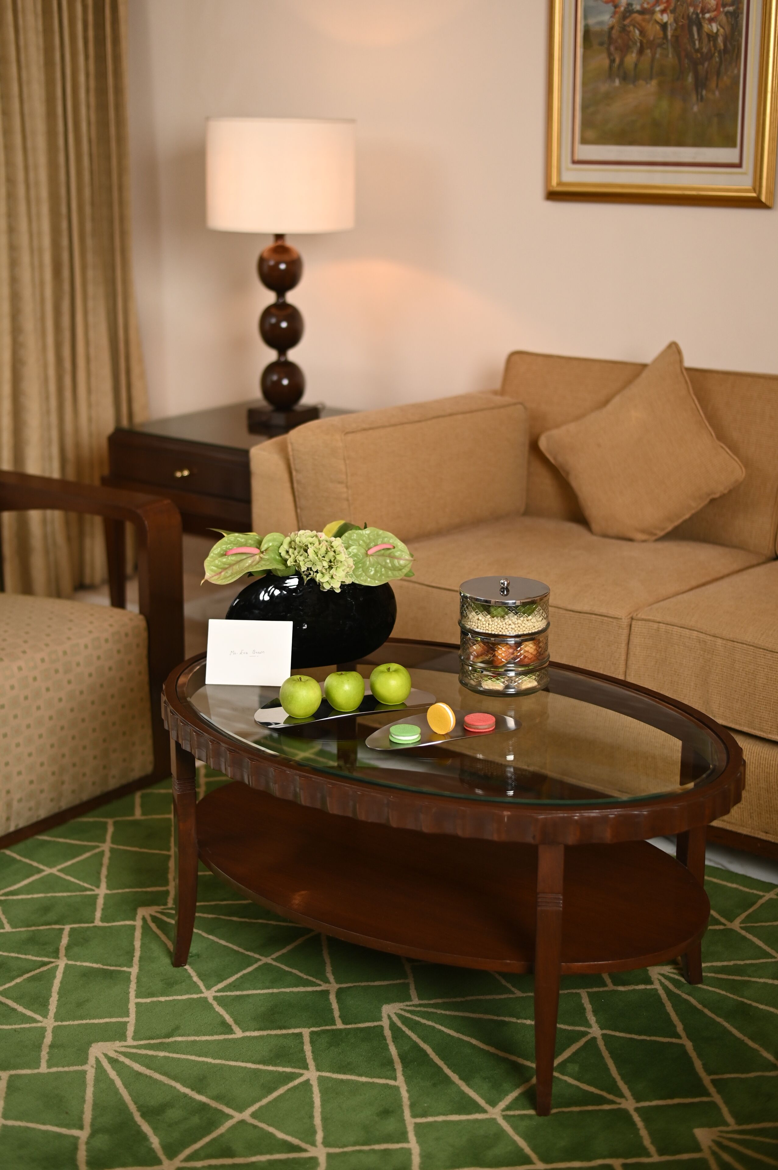 A room with a round glass coffee table, a sofa, a lamp, and a painting on the wall.