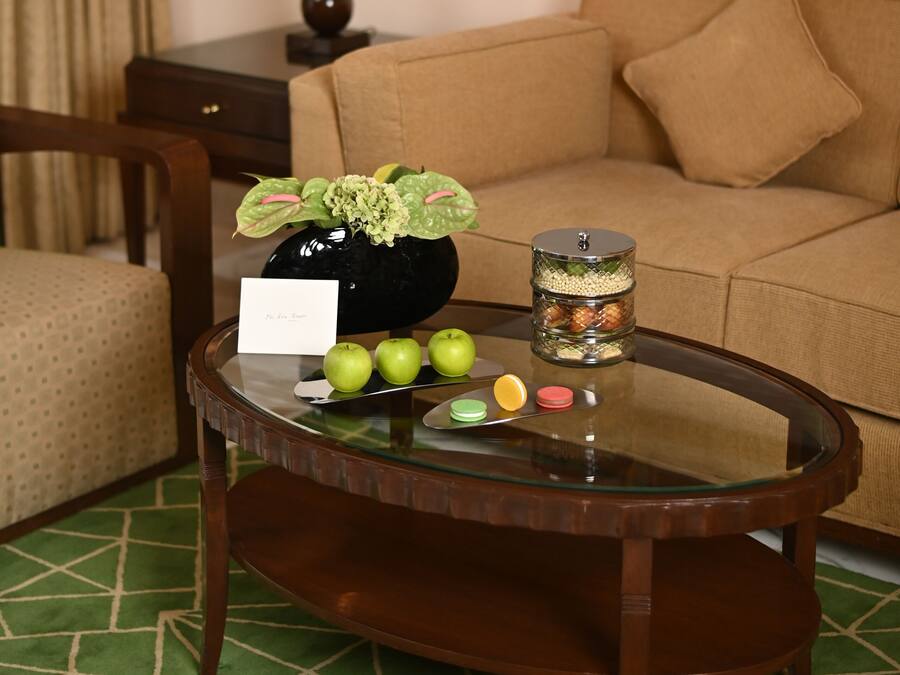 A room with a round glass coffee table, a sofa, a lamp, and a painting on the wall.