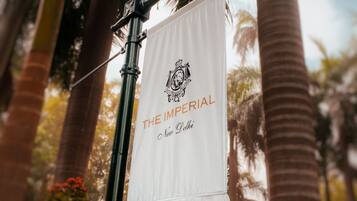 A street lamp with a banner reading 'THE IMPERIAL New Delhi' in a tropical setting with palm trees.