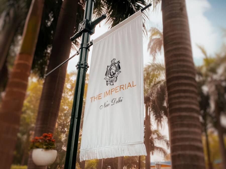 A street lamp with a banner reading 'THE IMPERIAL New Delhi' in a tropical setting with palm trees.