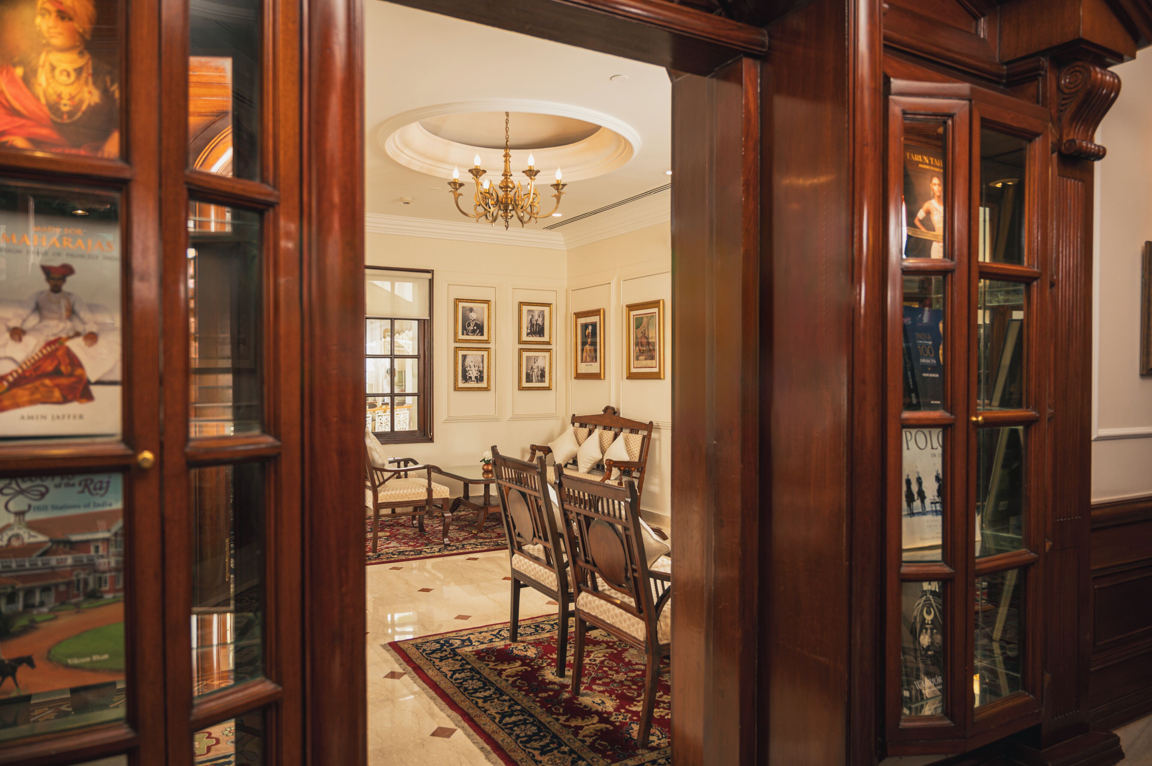 A room with a chandelier, framed pictures on the wall, a dining table with chairs, and a patterned rug.