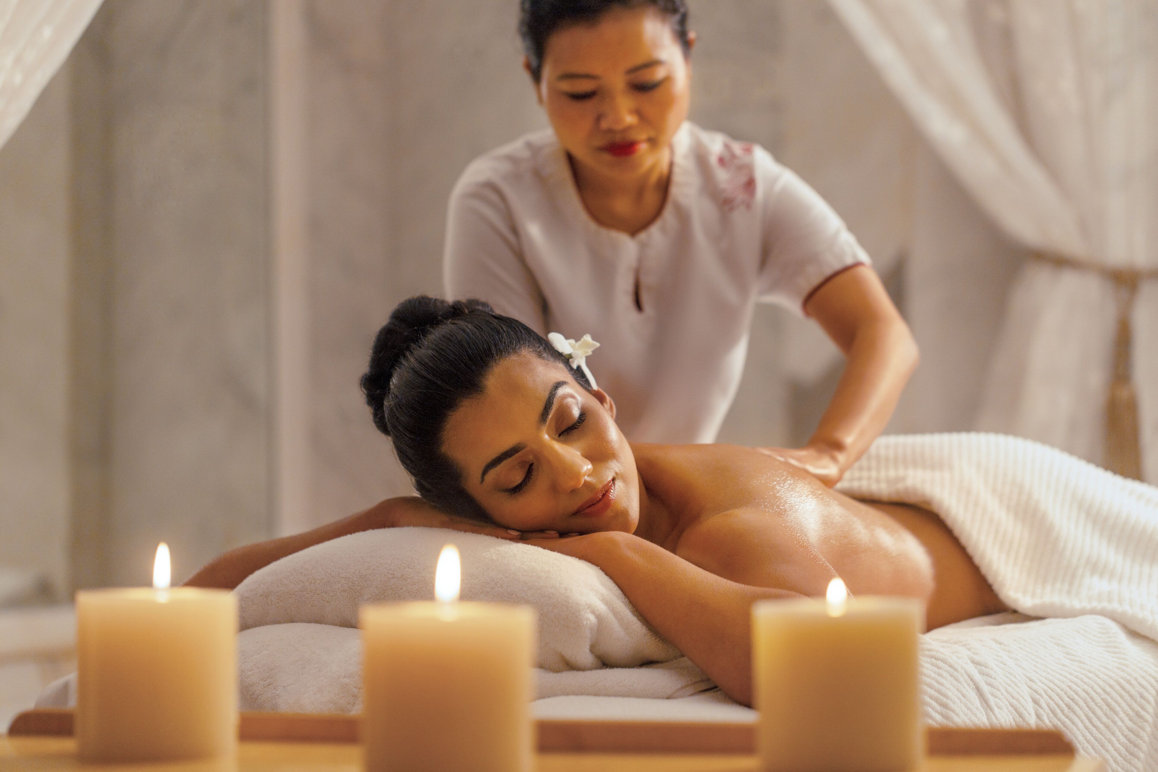 En spa-miljö med en massagebänk, ljus och en person som utför en massage.