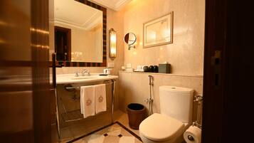 A bathroom with a sink, mirror, toilet, and a trash bin.