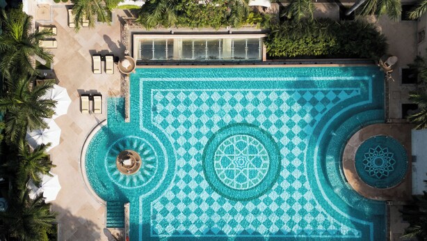 Vue aérienne d’une piscine d’un complexe hôtelier, avec ses motifs géométriques en mosaïque, ses chaises longues et ses parasols.