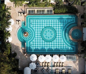 Vista aérea da piscina de um resort, com padrões geométricos em mosaicos, espreguiçadeiras e guarda-sóis.