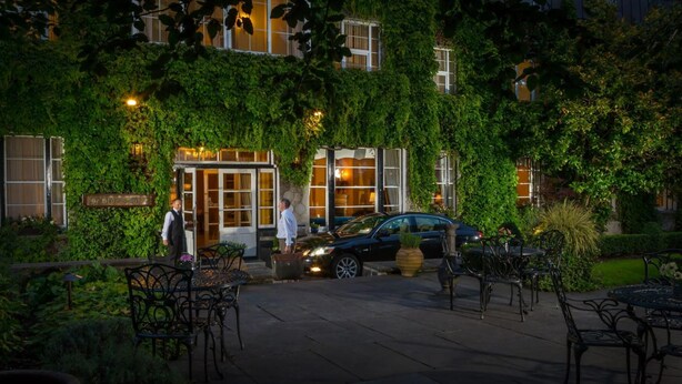 A hotel with ivy-covered walls, outdoor seating, and a car parked in front. - Old Ground Hotel (Ennis)