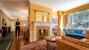 A well-appointed living room with a fireplace, a blue sofa, and a dining area with a table set for tea. - Old Ground Hotel (Ennis)