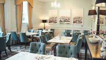 A dining area with multiple tables and chairs, a chandelier, and artwork on the walls.