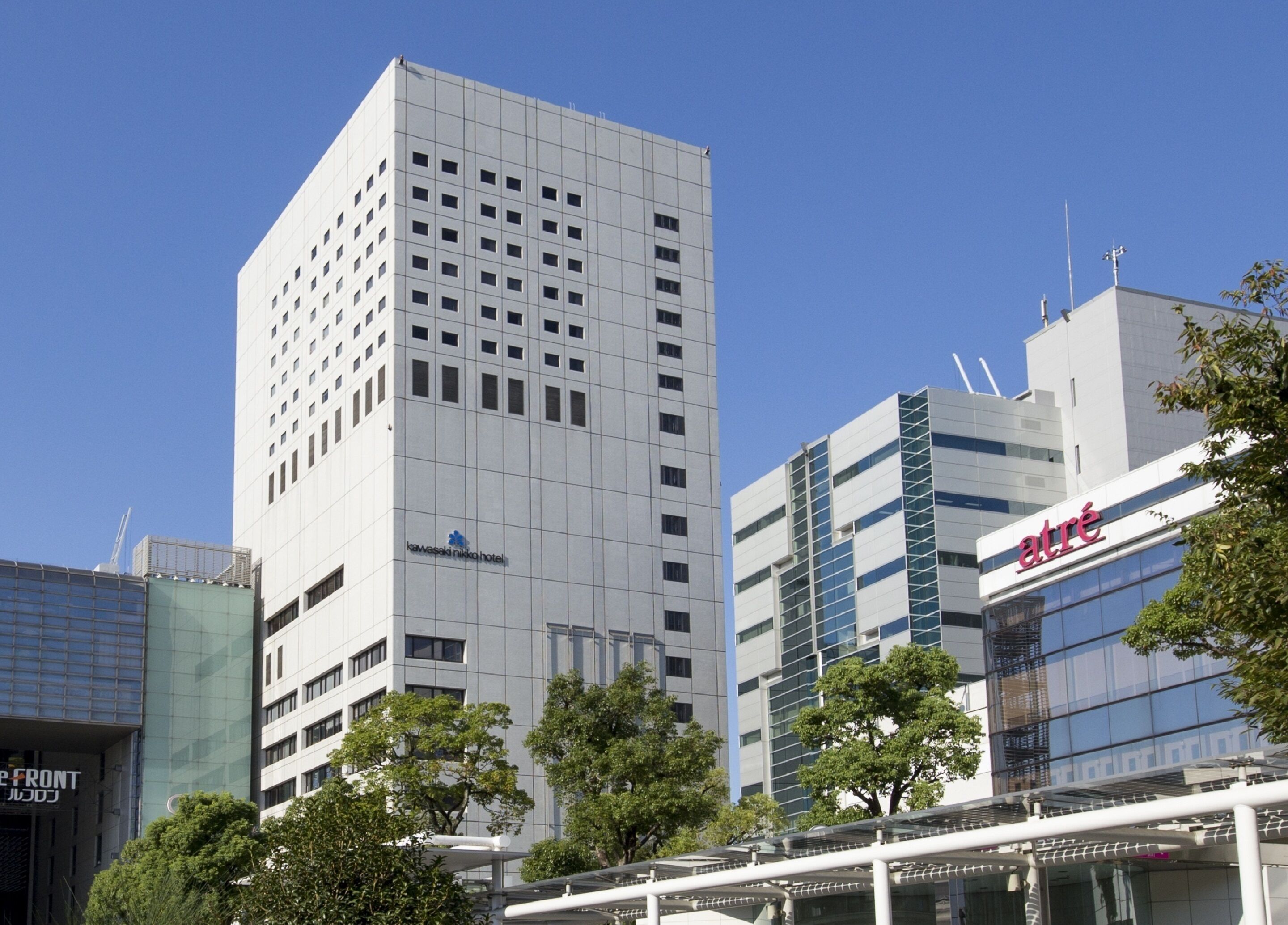 A modern hotel building with a grid-like facade, a visible sign for 'Kawasaki Nikko Hotel', and a glass-fronted building with 'atre' signage.