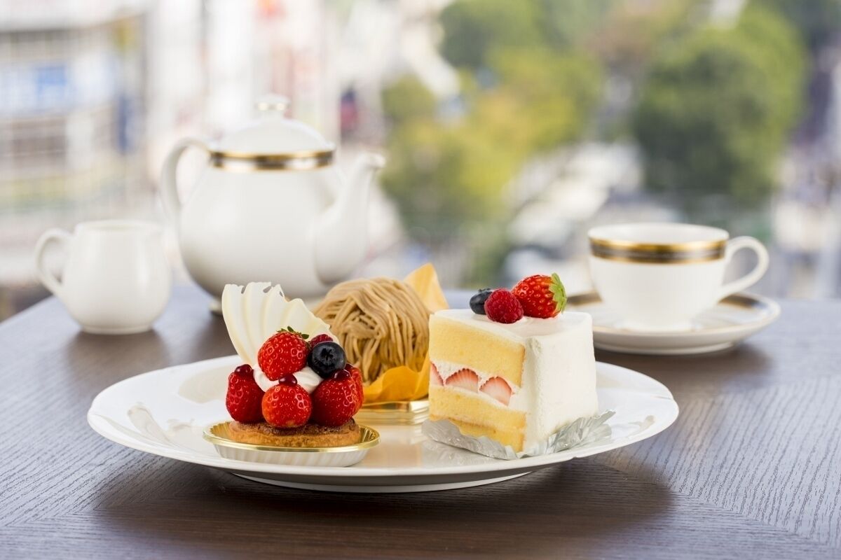 A table with a white teapot, a cup, and a plate with a slice of cake and berries.