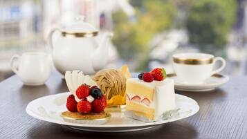 A table with a white teapot, a cup, and a plate with a slice of cake and berries.