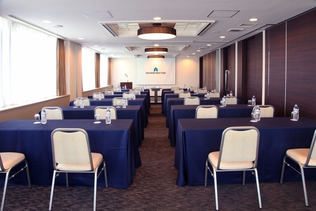 A conference room with rows of tables and chairs, a podium, and a presentation screen.