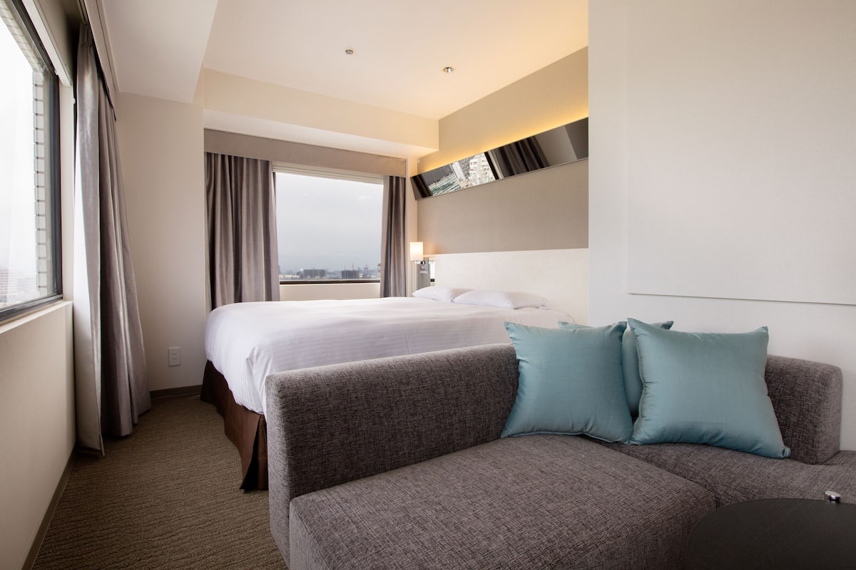 A hotel room with a bed, a sofa, and a large window.