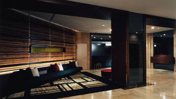 A modern lobby with a wooden slatted wall, a seating area with cushions, and a patterned carpet.