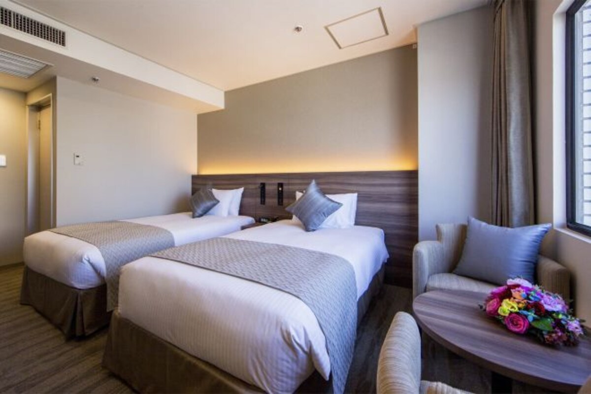 A hotel room with two beds, a sofa, and a small table with flowers.