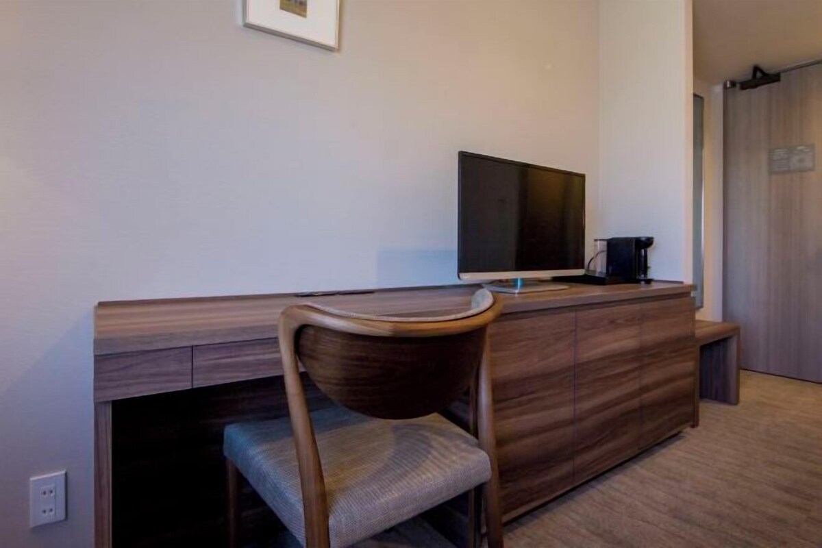 A modern room with a wooden desk, a flat-screen TV, and a coffee maker.
