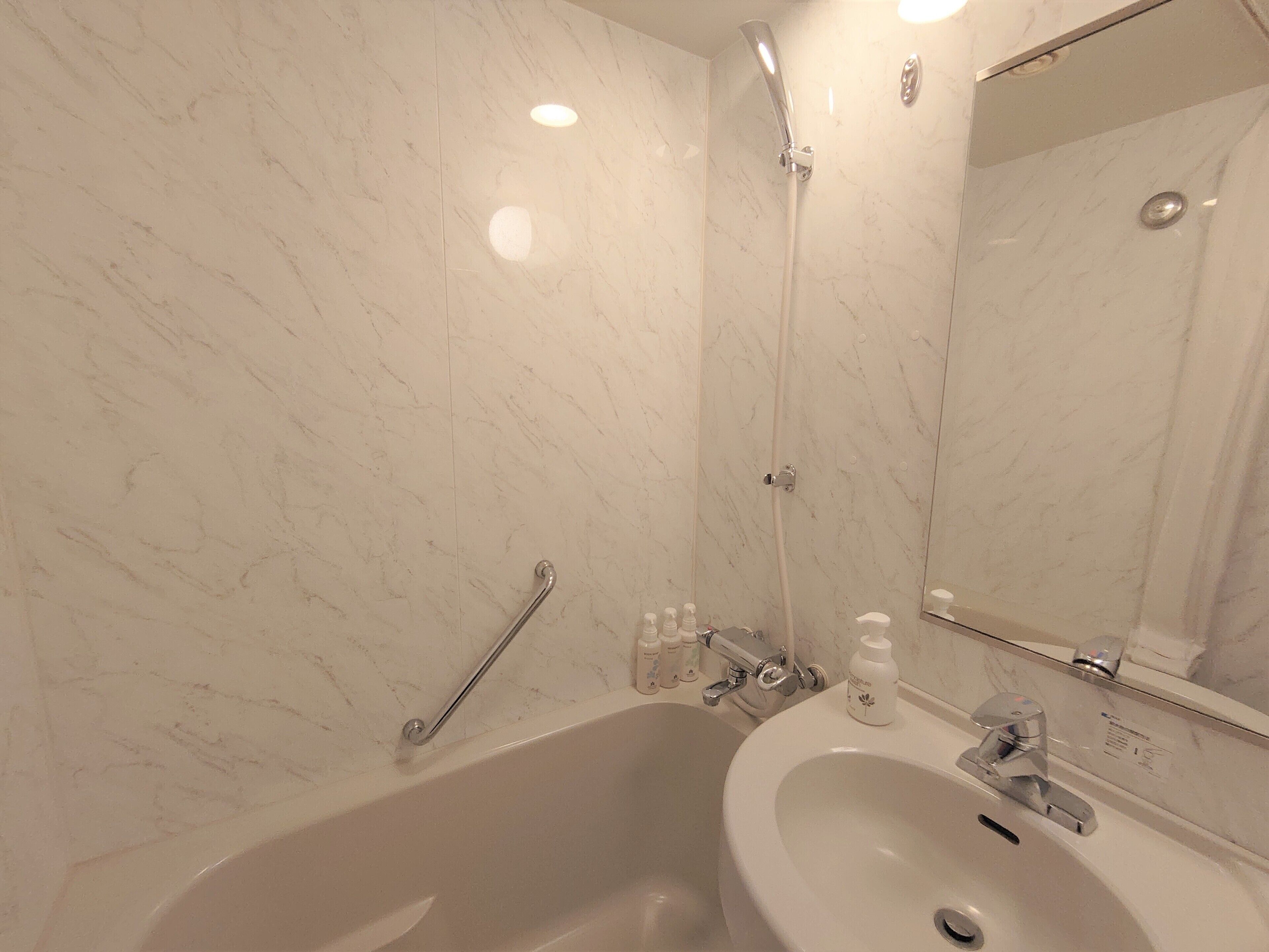 A bathroom with a marble wall, a bathtub, a sink, and a mirror.