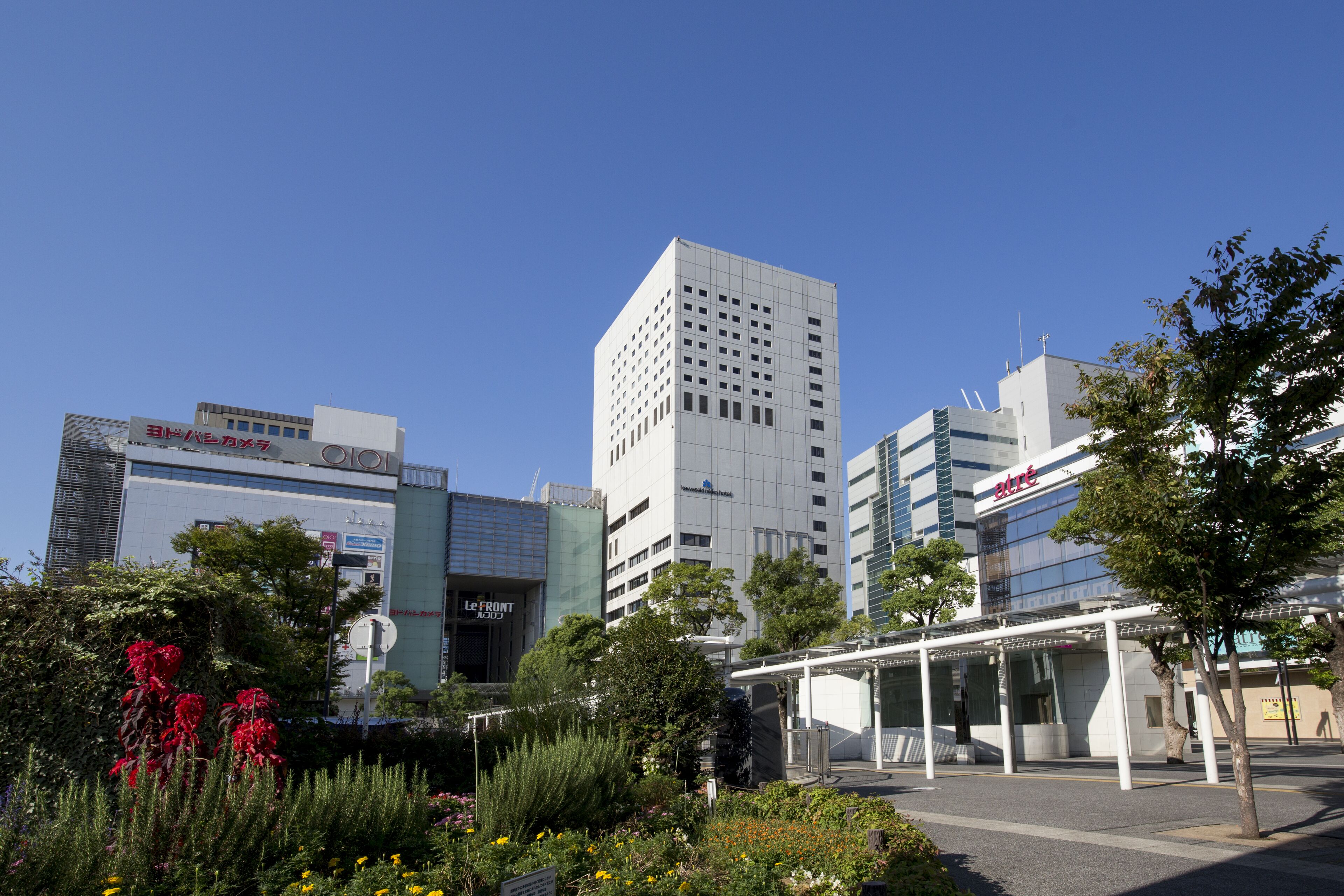 A modern urban area with tall buildings, a covered walkway, and a landscaped garden with various plants and flowers.