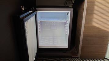 Un refrigerador compacto con compartimento congelador, en una habitación con piso de madera y área alfombrada.