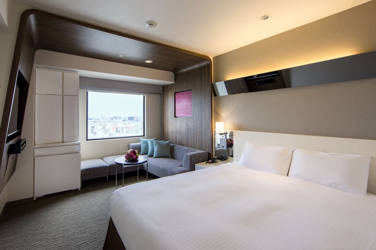 A hotel room with a large bed, a sofa, a small table, a desk, and a wardrobe.