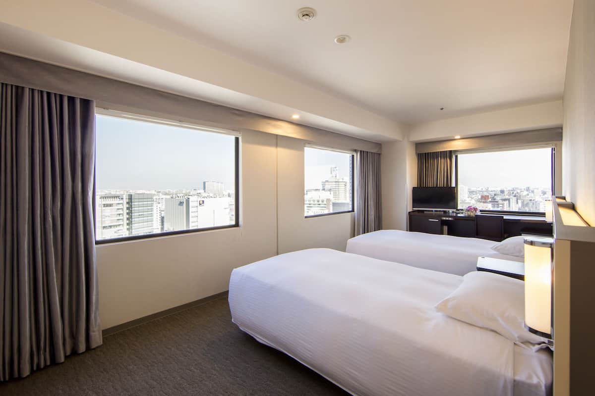 A hotel room with two beds, a desk, and a TV.