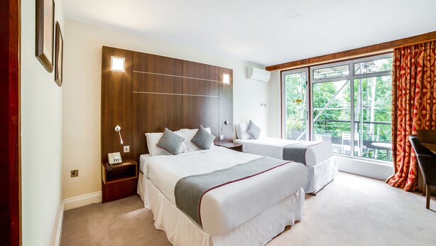 Une chambre d’hôtel avec deux lits, une grande fenêtre et une vue sur la verdure environnante.