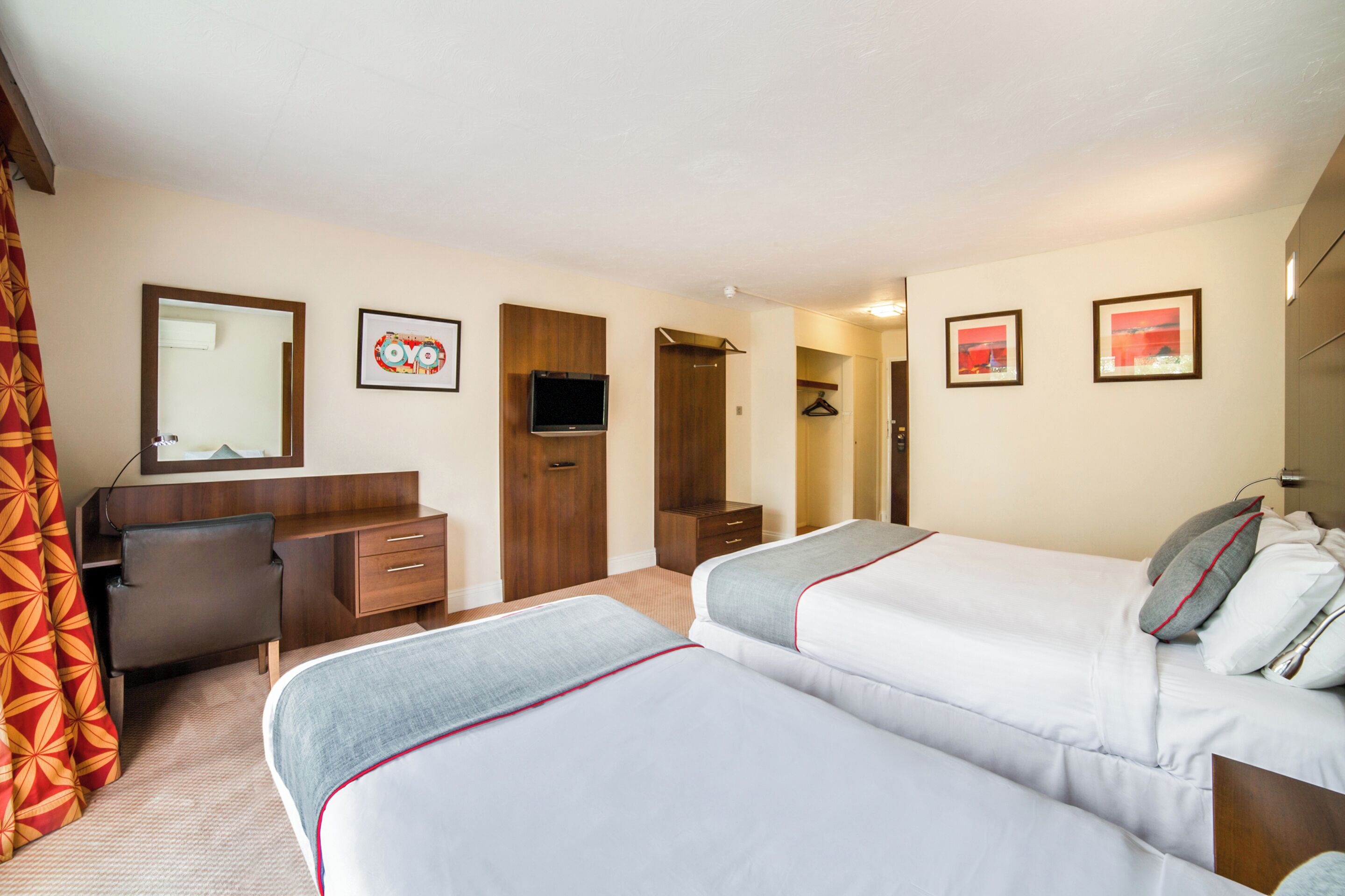 Ein Hotelzimmer mit zwei Betten, einem Schreibtisch, einem Spiegel und einem Fernseher.