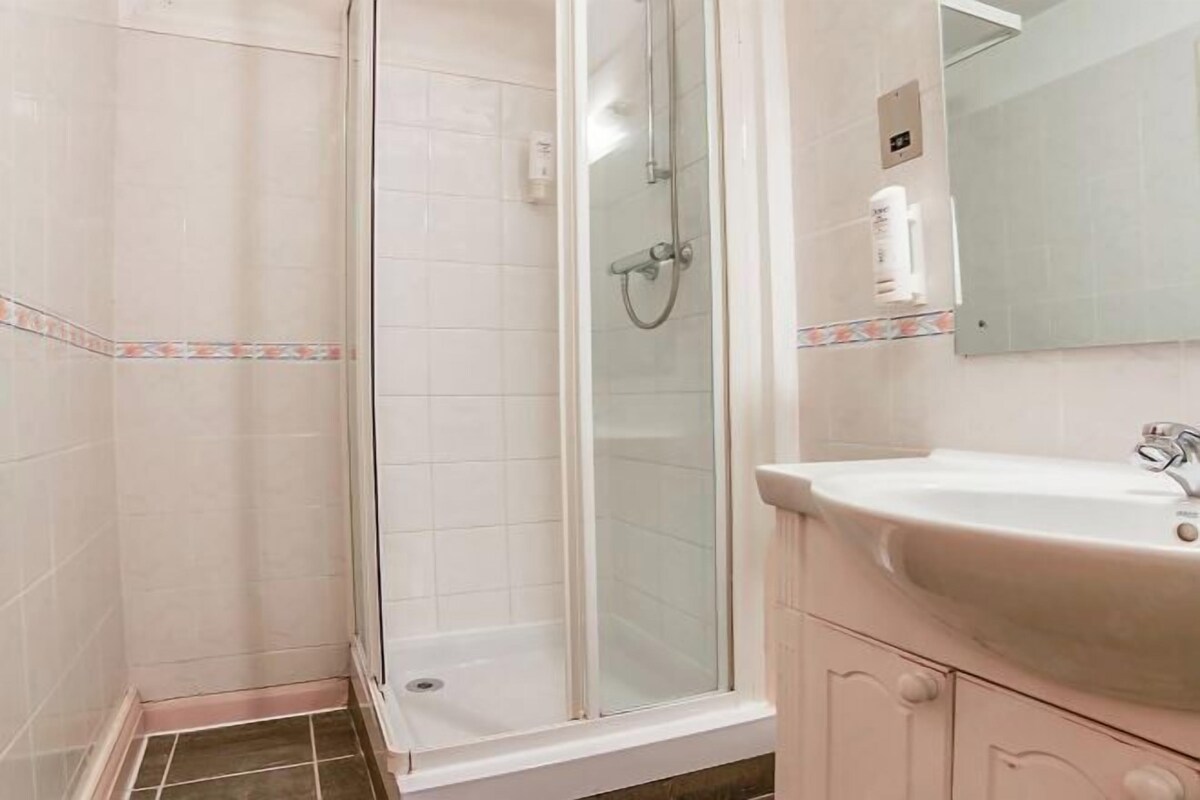 A bathroom with a glass-enclosed shower, a sink with a mirror, and a tiled floor.