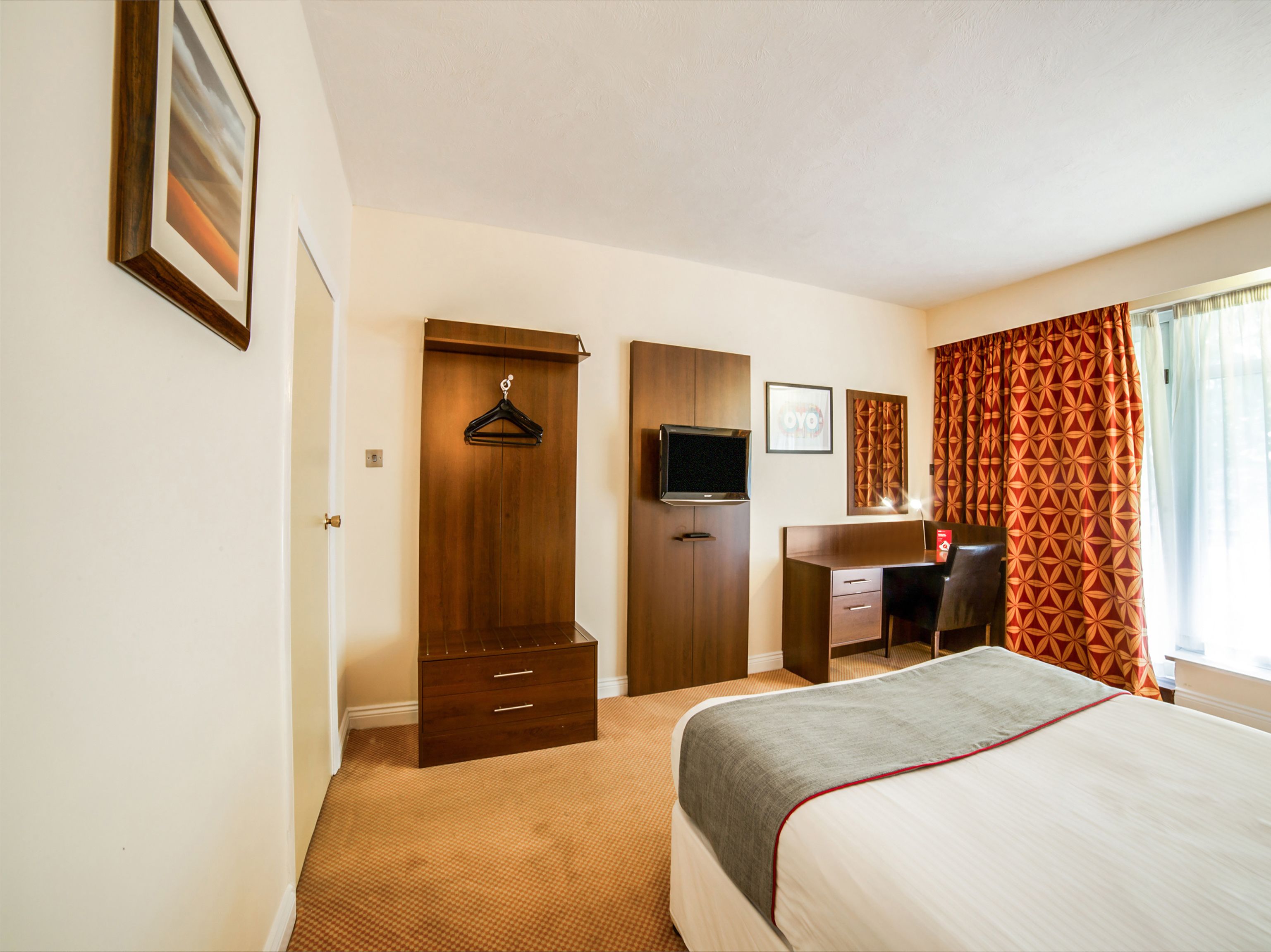 A hotel room with a bed, a desk, a TV, and a wardrobe.