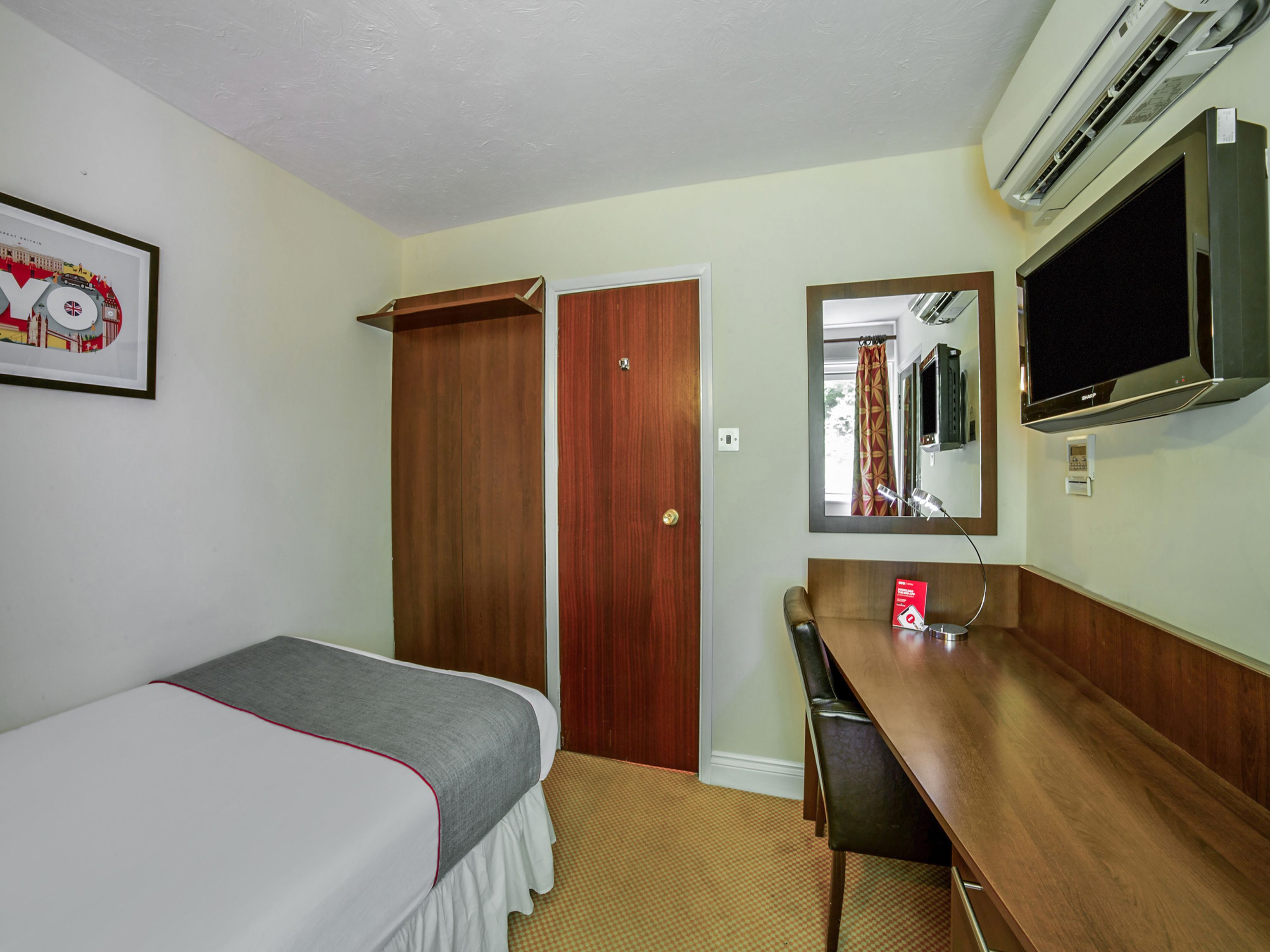 A hotel room with a bed, a desk, a mirror, and a wardrobe.