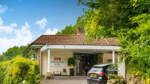L’entrée d’un hôtel, avec une voiture garée devant, une enseigne indiquant « OYO BRIDGE HOUSE HOTEL » et un mur de pierre sur la droite.