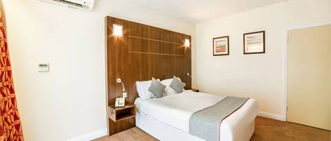 A hotel room with a large bed, a bedside table with a lamp, an air conditioning unit, and a wall-mounted phone.