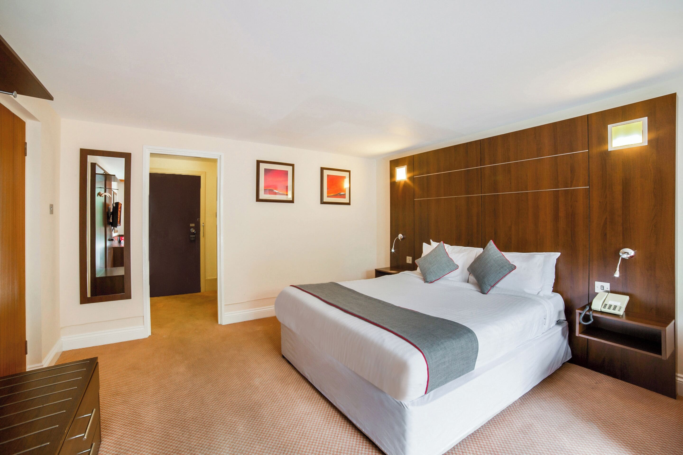 A hotel room with a large bed, a bedside table with a phone, and a mirror on the wall.