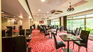 Une salle à manger d’hôtel avec des tables et des chaises, une moquette rouge et de grandes fenêtres donnant sur un paysage verdoyant.