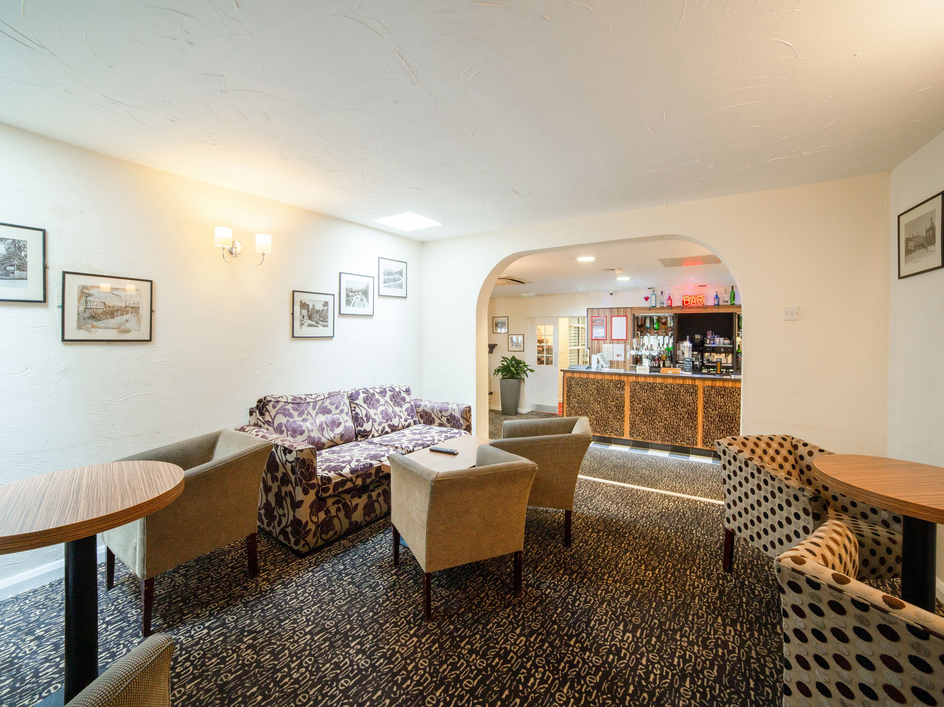 A hotel lobby with a bar area, seating arrangements, and framed pictures on the walls.